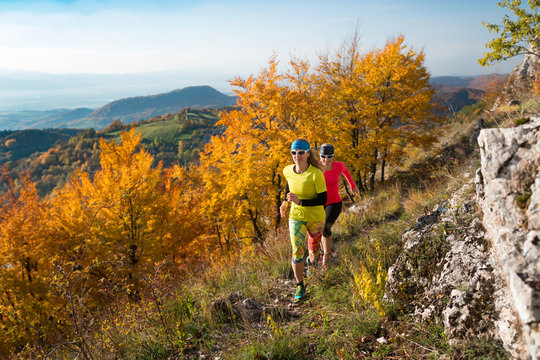 two young women running on the rocky track in autumn mountains 