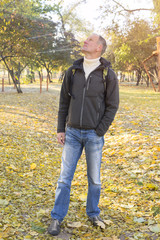 Attractive man with backpack relaxing in a autumn park, stands a