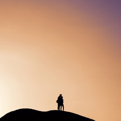 Silhouette of unidentified couple on a rock against orange sky.