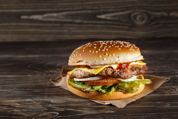 Cheese burger with grilled meat, cheese, tomato, on craft paper on wooden surface. Fast food template. Cheeseburger