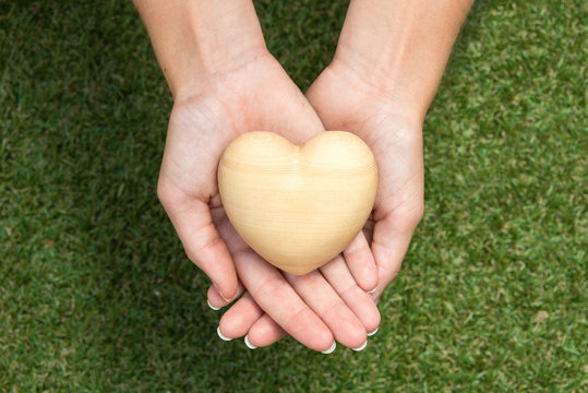 Wooden heart held by two crossed hands above gras