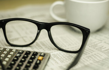glasses , a cup of coffee and calculator on a newspaper