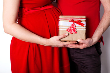 Anticipation. Pregnant couple in red with gift
