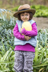 kid gardening concept - happy preschool child enjoying holding tight a squash with gardener straw hat on in home vegetable garden in autumn season, outdoors view