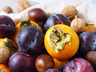 Fototapeta premium Persimmons with purple plums, chestnuts and walnuts. Fall still life