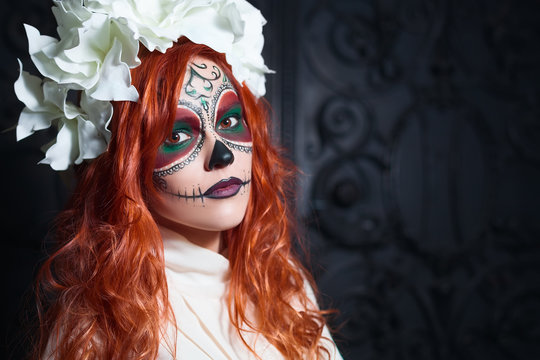 Portrait of young redhead woman with Halloween sugar skull makeup looking at camera. Close up. Dark backgraund. Copy space, free text. 