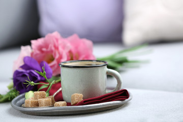 Cup of coffee with flowers on tray on sofa in room