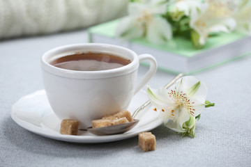Cup of coffee with lump sugar and flowers on sofa