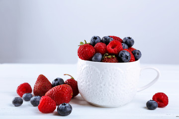 Tasty ripe berries in cup on gray background