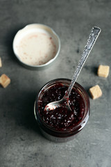 A jar of tasty jam, a spoon and crackers on grey background
