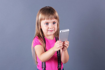 Fototapeta premium Beautiful little girl with mobile phone, on grey background