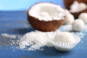 Candies in coconut flakes and fresh coconut on color wooden background