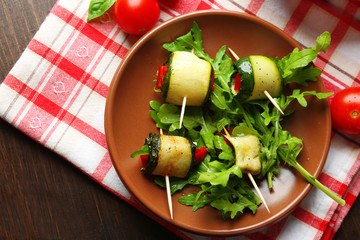 Zucchini rolls with cheese, bell peppers and arugula on plate, close-up, on table background