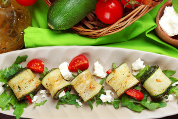 Zucchini rolls with cheese, bell peppers and arugula on plate, close-up, on table background