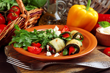 Zucchini rolls with cheese, bell peppers and arugula on plate, close-up, on table background