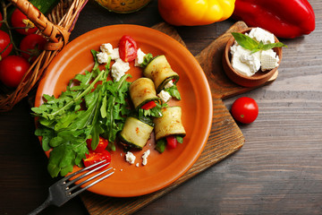 Zucchini rolls with cheese, bell peppers and arugula on plate, close-up, on table background