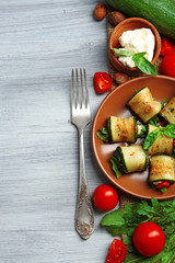 Salad with arugula and zucchini rolls on plate, on table background