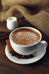 Cup of coffee with cream and coffee beans on wooden background