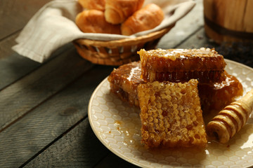 Honeycombs on plate, hot buns in basket on wooden background