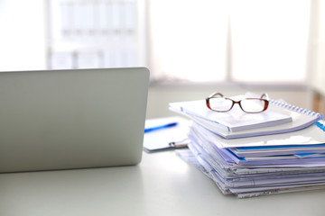 Laptop with stack of folders on table on white background