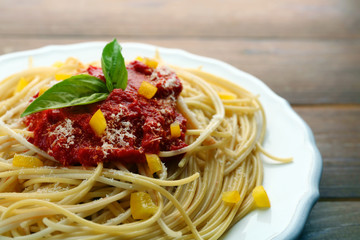 Spaghetti with tomato sauce, paprika and cheese on white plate, on color wooden background