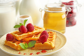 Sweet homemade waffles with fresh raspberries on plate, on light background