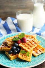Sweet homemade waffles with forest berries and sauce on table background