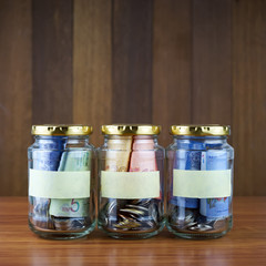 Image of money in three clear bottles with blank labels against blurred wooden background. Saving concept.