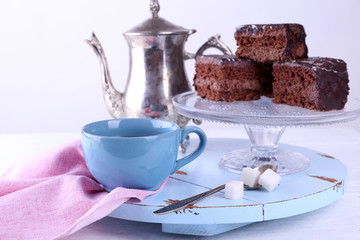 Served table with a teapot, a cup of tea and chocolate cakes on blue and white background close-up