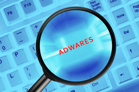 Magnifying glass on computer keyboard with "Adwares" word.