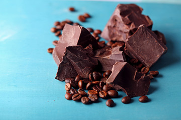 Black chocolate pieces and coffee grains on color wooden background