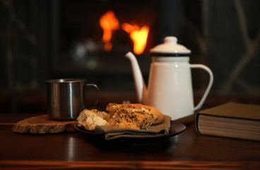 Teapot and mugs on vintage wooden table. Fireplace as background