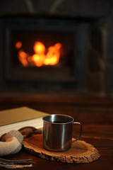 Book and mug with hot drink on vintage wood table. Fireplace as background
