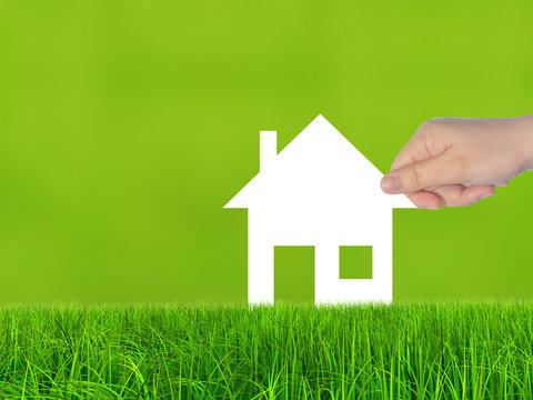 Conceptual white paper house symbol held in hand in green grass