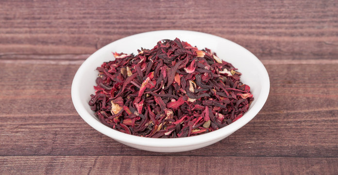 Dried red hibiscus tea leaves in white bowl over wooden background