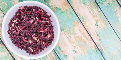 Obraz na płótnie Canvas Dried red hibiscus tea leaves in white bowl over wooden background