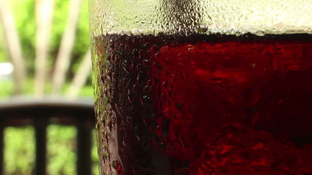 Medium close up of a glass of cola-colored fizzy drink with indistinct chair
