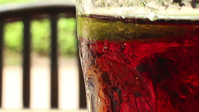 Close up of a glass of cola-colored fizzy drink with indistinct chair, backgr
