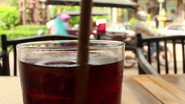 Close up of a glass of cola-colored fizzy drink with Asian tuk tuks passing i
