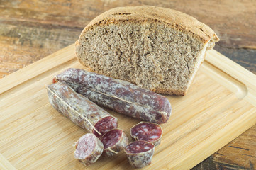 Pane nero e salamino, salame affettato su tagliere con pane scuro, coltello per salumi