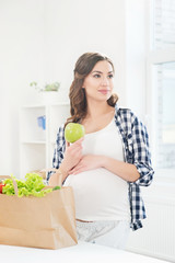 Beautiful pregnant woman in the kitchen with shopping bag and apple.