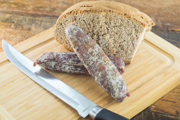 Pane nero e salamino, salame affettato su tagliere con pane scuro, coltello per salumi
