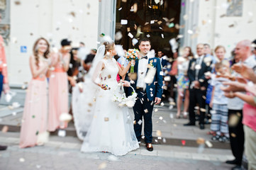 wedding couple come out from church under petals of roses. blur