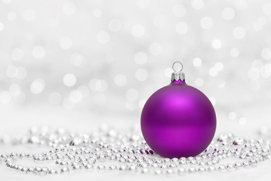 Purple Christmas ball with metalic beads. Bokeh with glow effect on white background. Copyspace for your greeting or wishes