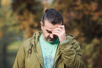 Worried man outside in a park, hand covering face, fall season