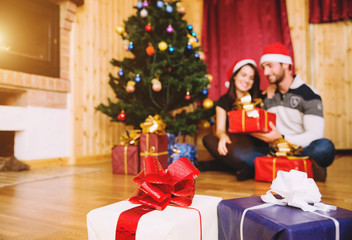 couple of lovers opens gifts during Christmas night under the Christmas tree and near the fireplace - focus on the gifts - caucasian people - people, christmas and lifestyle concept