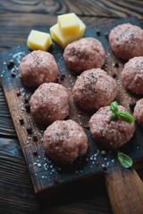 Raw meatballs on a rustic wooden chopping board, selective focus