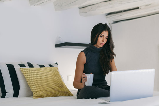 Beautiful Brunette Woman Using a Laptop and Drinking Coffee on B