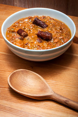 Bowl of delicious homemade beans and sausage in a rustic kitchen , on a wooden table with a wooden spoon in the frame.