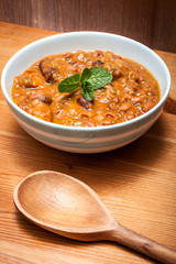 Bowl of delicious homemade beans and sausage in a rustic kitchen , on a wooden table with a wooden spoon in the frame and some mint leaves in the bowl